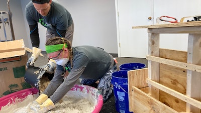 Homeland Hempcrete’s Matt Marino pouring hemp hurd into a water and lime mixture as the business’ Sam Marino, Matt’s wife, mixes it all together.