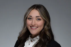 Professional headshot of a smiling woman with long brown hair wearing a black blazer and white blouse