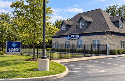 Ascend Dispensary brick building exterior with logo sign, black fence, and landscaping
