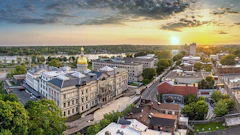 Aerial sunset view of downtown with golden-domed state capitol building surrounded by historic architecture and tree-lined streets along a river.