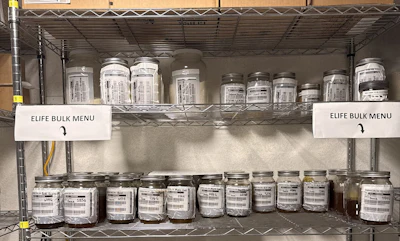 Shelving unit displaying multiple glass jars with ELIFE bulk products and white menu labels