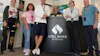 Six team members pose together with a Still River Wellness branded banner at an indoor event