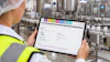 Factory worker in safety gear viewing software dashboard on tablet in industrial manufacturing facility