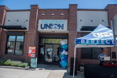 Perfect Union cannabis retail storefront with blue and white branding, entrance signage, and promotional tent display