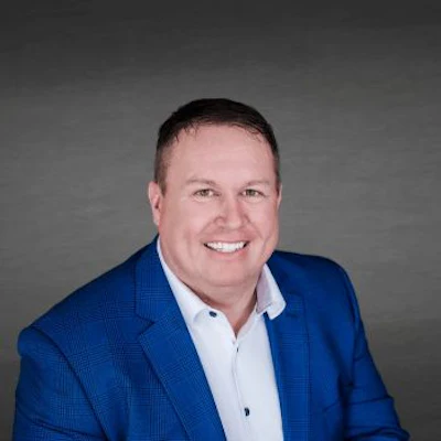 Professional headshot of a smiling man in a blue blazer and white shirt against a gray background