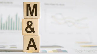 Wooden blocks spelling M&A stacked on business documents with financial charts