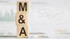 Wooden blocks spelling M&A stacked on business documents with financial charts
