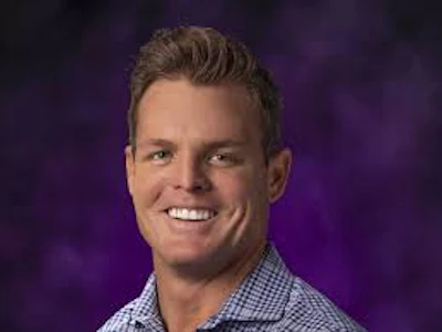 Professional headshot of a smiling man in a checkered shirt against a purple gradient background