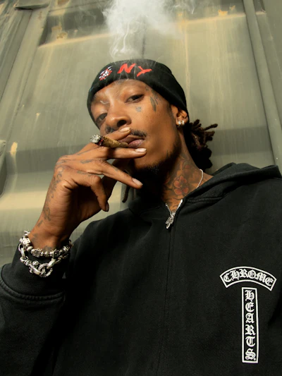 Person wearing black Carhartt WIP hoodie with silver chain bracelet and rings, smoking cigar indoors